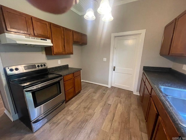 kitchen with light wood finished floors, brown cabinetry, electric stove, dark countertops, and under cabinet range hood