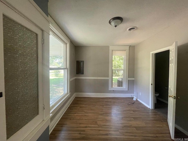 empty room with dark wood-style flooring, visible vents, and baseboards