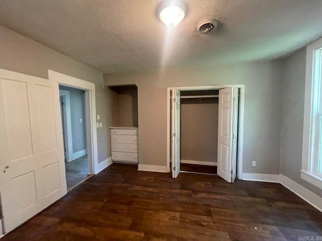 unfurnished bedroom with a closet, wood finished floors, visible vents, and baseboards