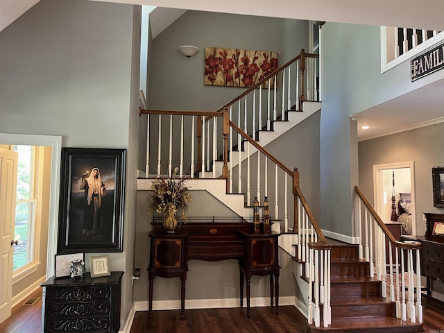 staircase featuring visible vents, a towering ceiling, ornamental molding, wood finished floors, and baseboards