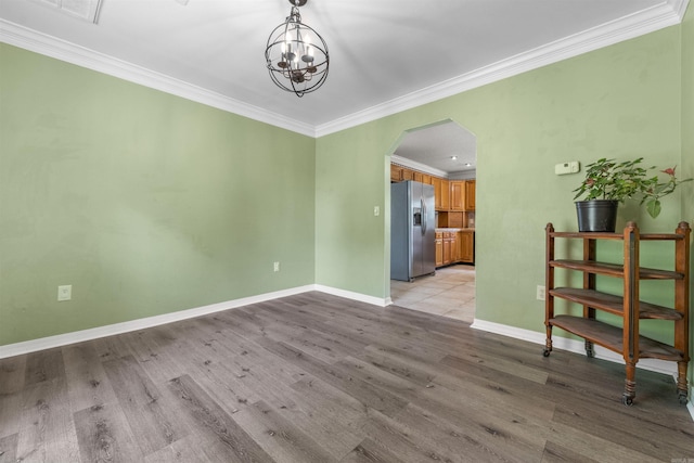 unfurnished room with arched walkways, light wood-style flooring, an inviting chandelier, ornamental molding, and baseboards