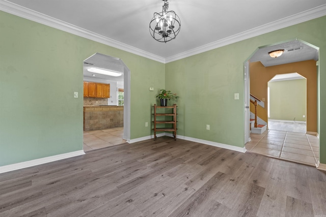 spare room featuring a notable chandelier, ornamental molding, and light wood-type flooring