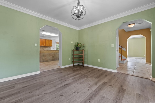 spare room featuring arched walkways, ornamental molding, stairs, and light wood-style flooring