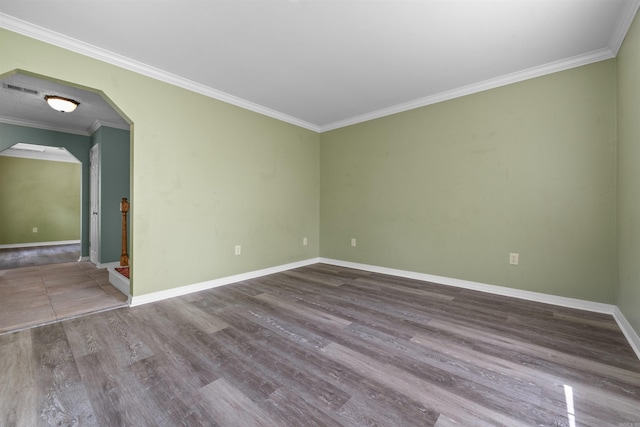 empty room with baseboards, visible vents, arched walkways, ornamental molding, and wood finished floors