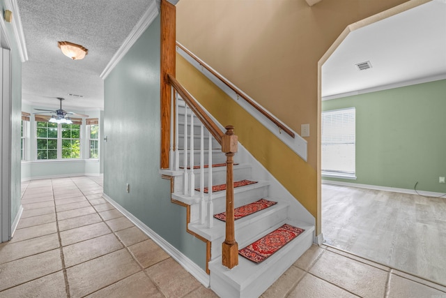 stairway with a ceiling fan, a textured ceiling, baseboards, and crown molding