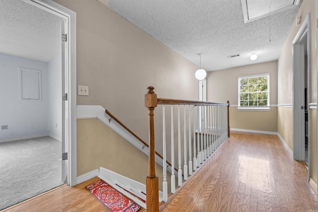 stairway with a textured ceiling, wood finished floors, visible vents, baseboards, and attic access