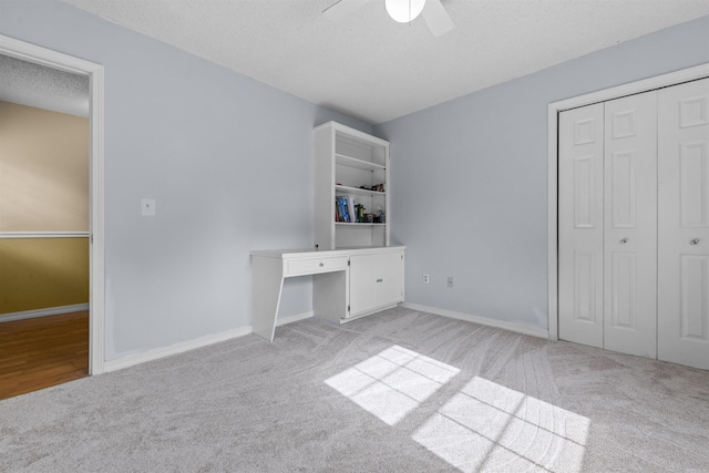 unfurnished bedroom featuring ceiling fan, light colored carpet, built in desk, a closet, and a textured ceiling