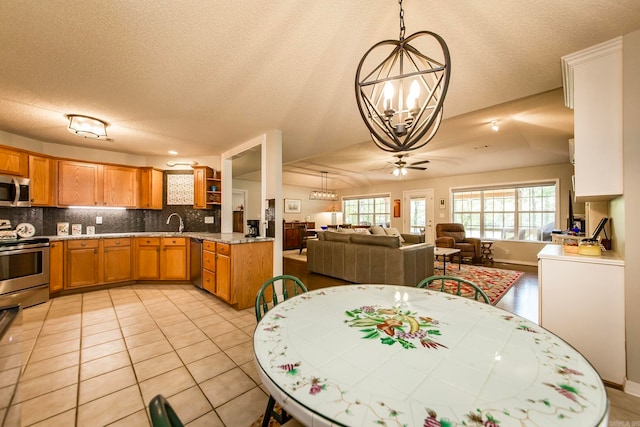 dining space featuring light tile patterned floors, ceiling fan with notable chandelier, sink, and a textured ceiling