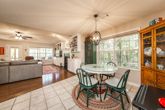 dining room with a textured ceiling, lofted ceiling, ceiling fan with notable chandelier, and light tile patterned floors