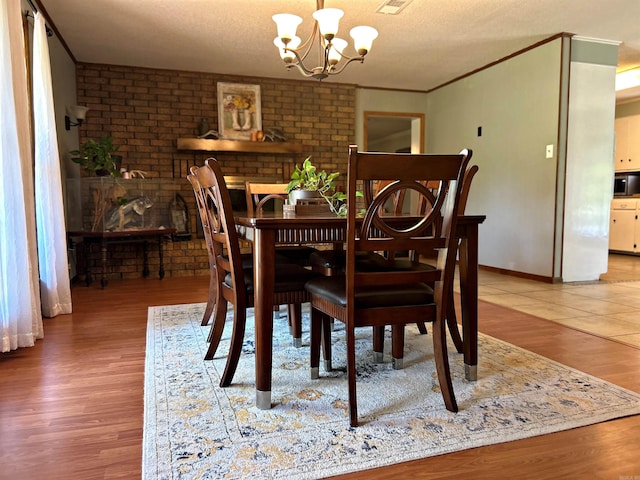 dining space with a textured ceiling, brick wall, an inviting chandelier, and wood-type flooring