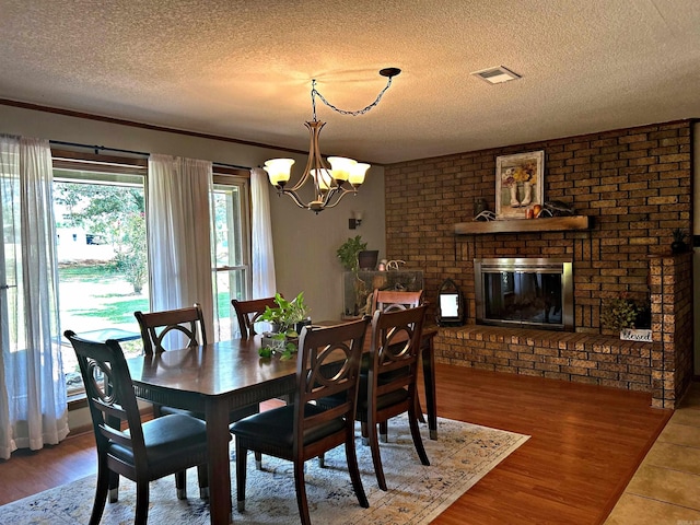 dining room featuring brick wall, a textured ceiling, a fireplace, a notable chandelier, and hardwood / wood-style flooring