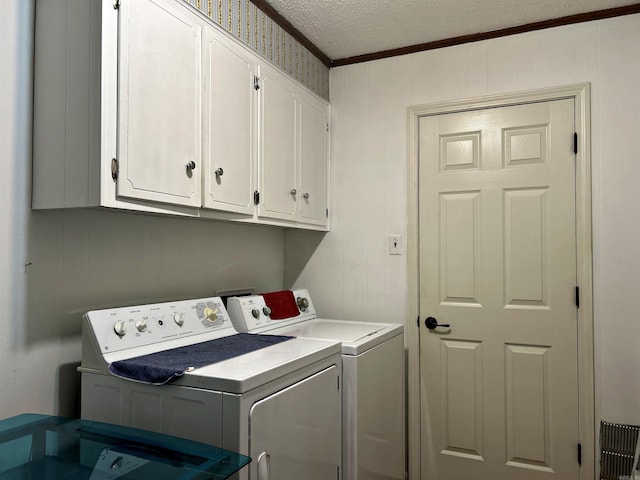 laundry room with crown molding, washing machine and clothes dryer, a textured ceiling, and cabinets