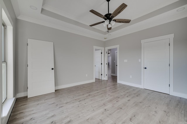 unfurnished bedroom with light wood-type flooring, a tray ceiling, and ceiling fan