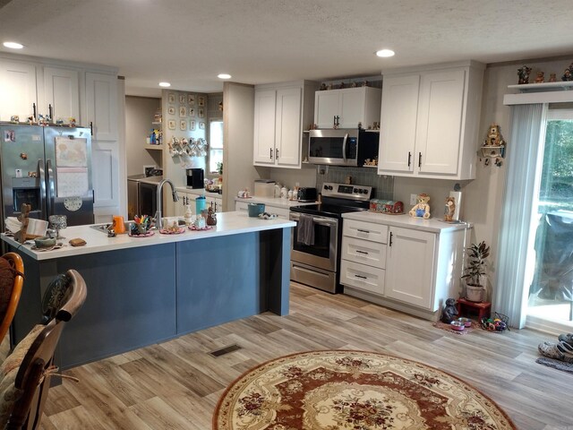 kitchen with light hardwood / wood-style floors, stainless steel appliances, decorative backsplash, and white cabinets