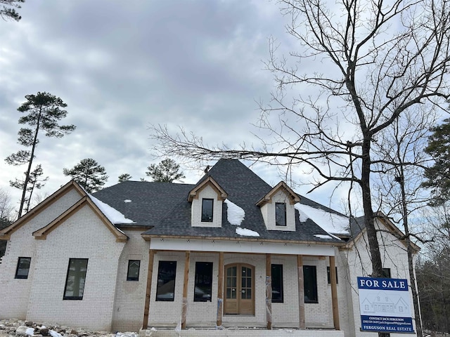 view of front of house with covered porch, a shingled roof, and brick siding