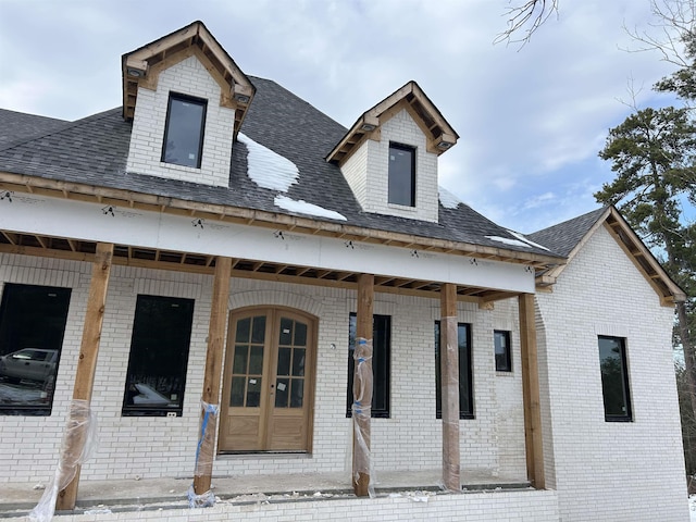 view of front of house featuring a shingled roof, a porch, and brick siding