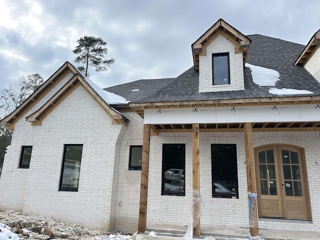 view of front of property featuring brick siding, french doors, and roof with shingles