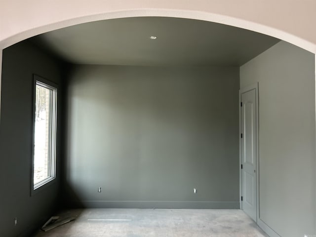 unfurnished room with a wealth of natural light, arched walkways, and baseboards