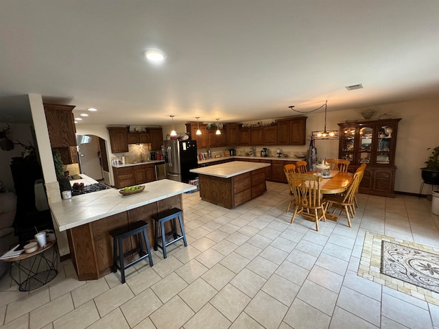 kitchen featuring stainless steel fridge, a breakfast bar area, light tile patterned floors, kitchen peninsula, and a center island