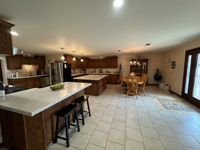 kitchen featuring backsplash, a chandelier, a kitchen island, stainless steel refrigerator with ice dispenser, and a kitchen bar