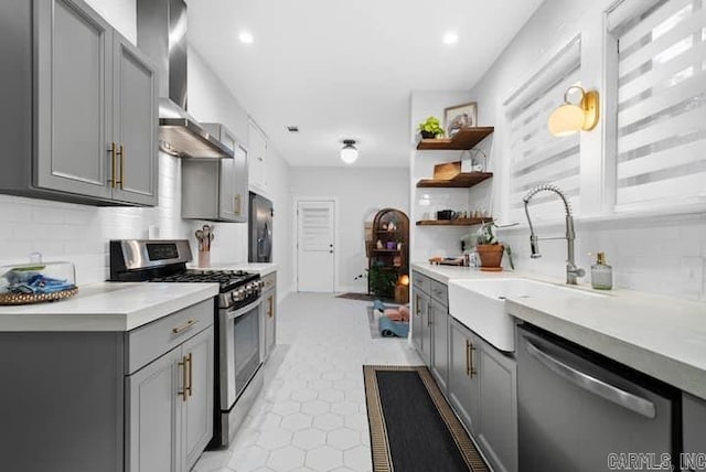 kitchen featuring backsplash, light tile patterned floors, stainless steel appliances, gray cabinets, and wall chimney range hood