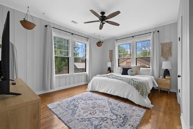 bedroom with ceiling fan, hardwood / wood-style flooring, ornamental molding, and multiple windows