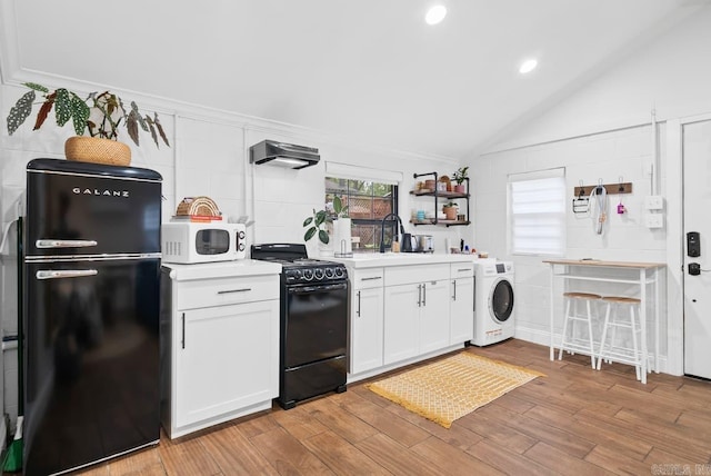 kitchen featuring light hardwood / wood-style flooring, vaulted ceiling, white cabinetry, washer / dryer, and black appliances