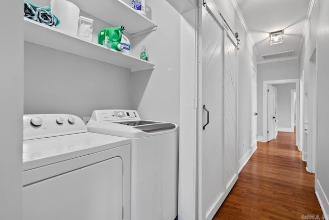 washroom featuring ornamental molding, a barn door, washing machine and dryer, and wood-type flooring