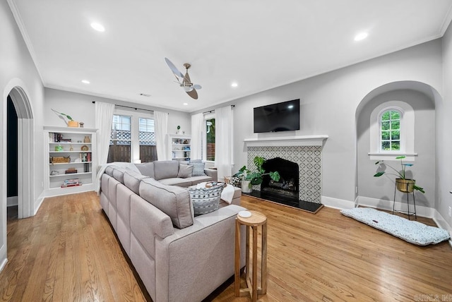 living room with ceiling fan, light hardwood / wood-style floors, a tile fireplace, and ornamental molding