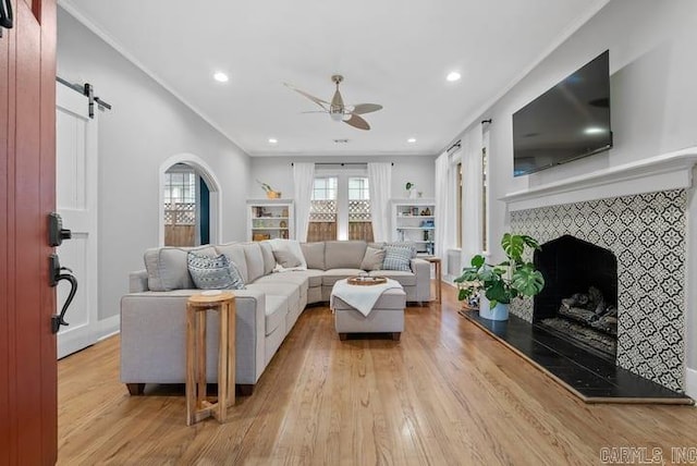 living room featuring ceiling fan, light hardwood / wood-style flooring, a barn door, a fireplace, and crown molding