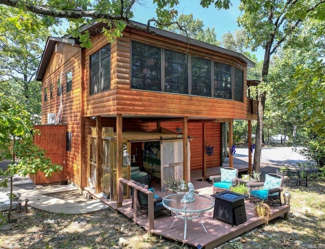 rear view of house with an outdoor fire pit, a wooden deck, and faux log siding