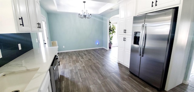 kitchen with light stone counters, decorative light fixtures, a tray ceiling, stainless steel appliances, and white cabinetry