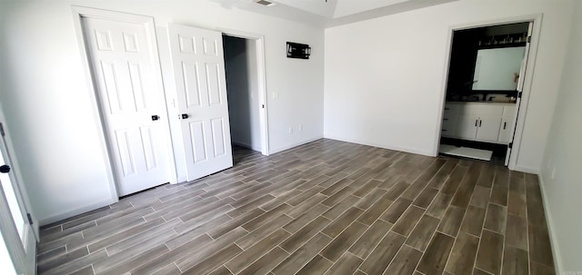 unfurnished bedroom featuring a closet, ensuite bath, and wood tiled floor