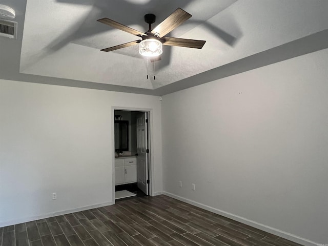 unfurnished bedroom with a tray ceiling, wood finish floors, visible vents, ensuite bathroom, and baseboards