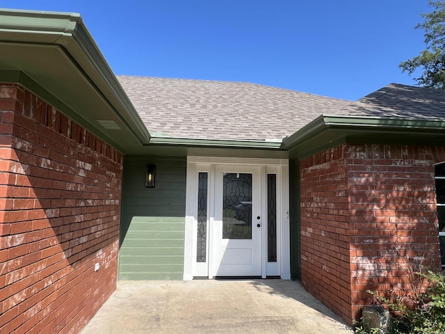 property entrance featuring a shingled roof and brick siding