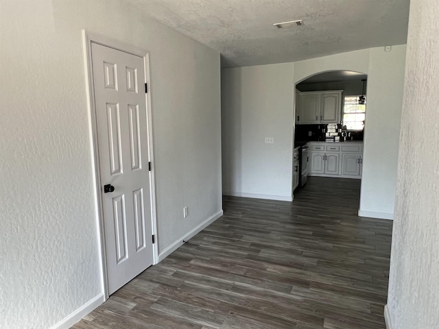 interior space featuring arched walkways, dark wood finished floors, a textured ceiling, and baseboards