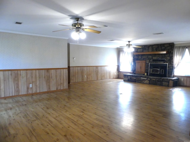 unfurnished living room with ceiling fan, hardwood / wood-style flooring, a stone fireplace, and crown molding