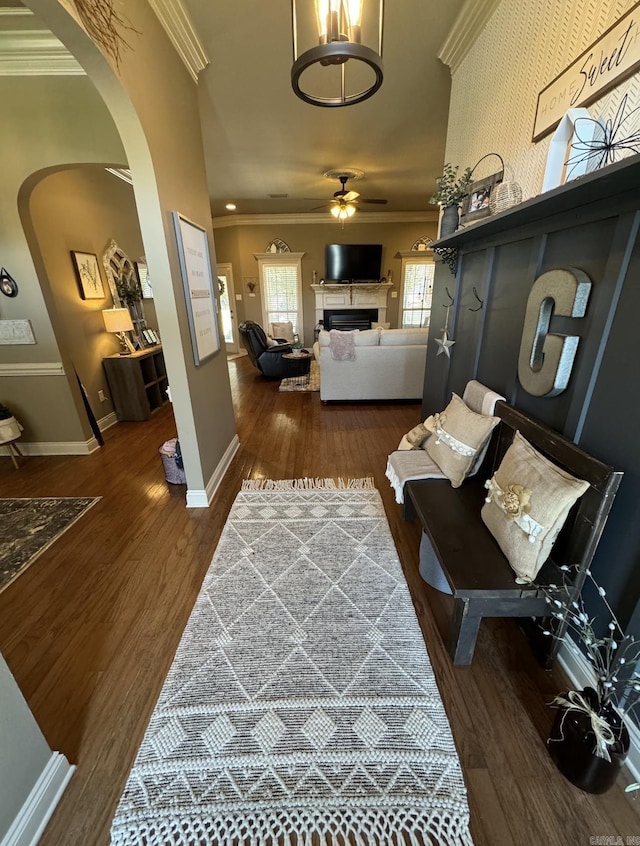 interior space with arched walkways, dark wood-style flooring, ornamental molding, a ceiling fan, and baseboards