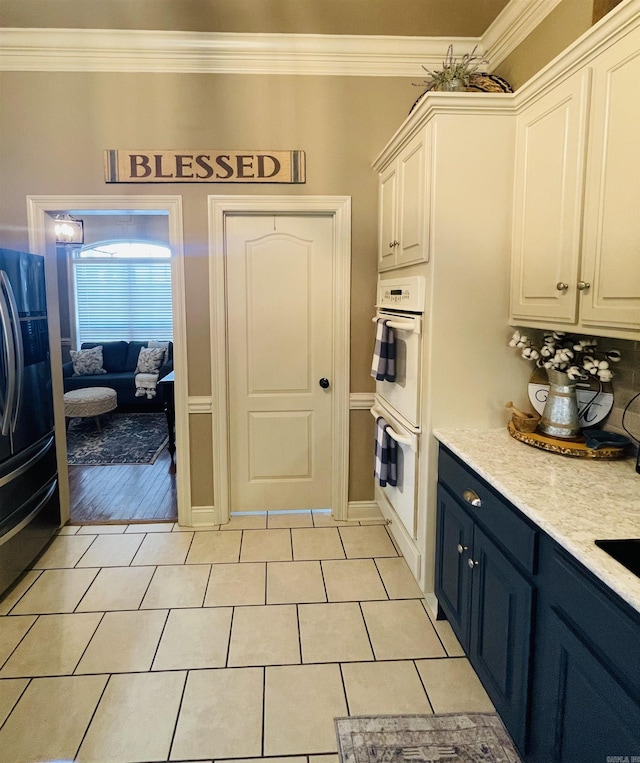 kitchen featuring white cabinets, light countertops, ornamental molding, blue cabinetry, and freestanding refrigerator