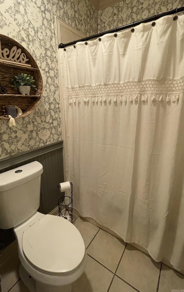 full bathroom with toilet, wallpapered walls, tile patterned floors, and wainscoting