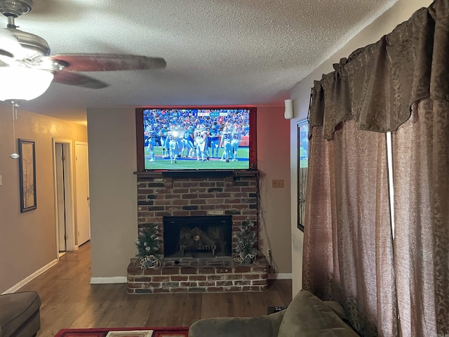 living room featuring ceiling fan, brick wall, hardwood / wood-style floors, a fireplace, and a textured ceiling