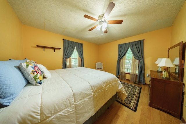 bedroom featuring a textured ceiling, ceiling fan, multiple windows, and wood-type flooring