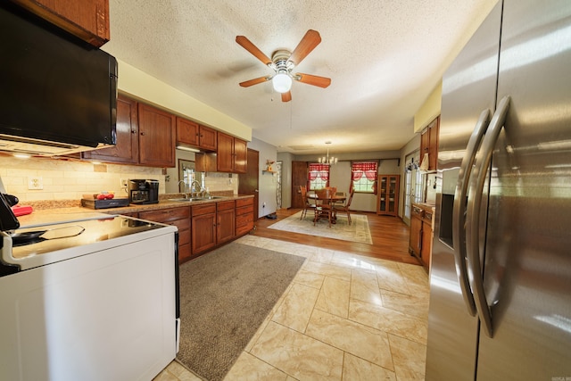 kitchen featuring decorative light fixtures, light hardwood / wood-style floors, tasteful backsplash, ceiling fan with notable chandelier, and stainless steel fridge