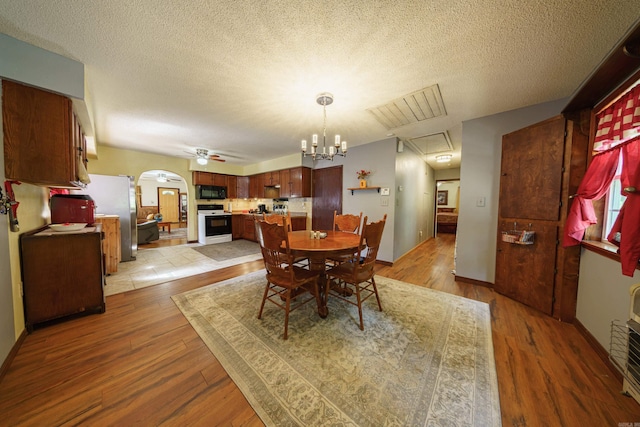 dining space with light wood-type flooring, ceiling fan with notable chandelier, and a textured ceiling