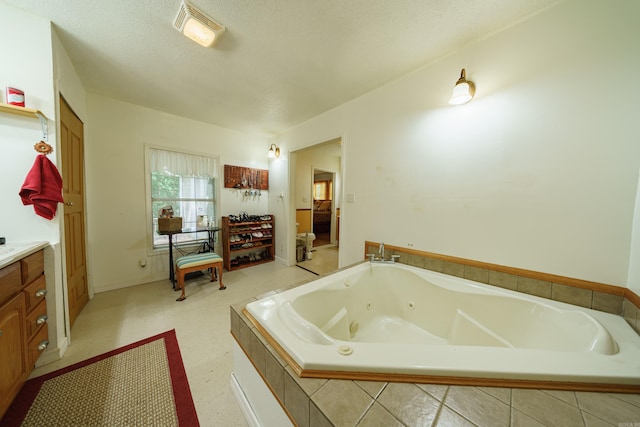 bathroom with a textured ceiling, tiled tub, vanity, and tile patterned floors