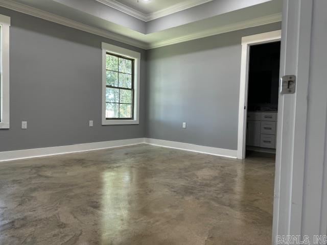 empty room with finished concrete floors, a raised ceiling, crown molding, and baseboards