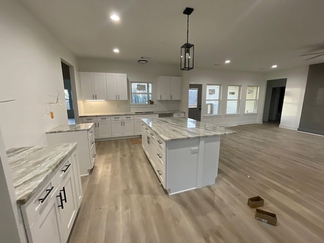 kitchen featuring pendant lighting, light hardwood / wood-style flooring, a center island, light stone countertops, and white cabinets