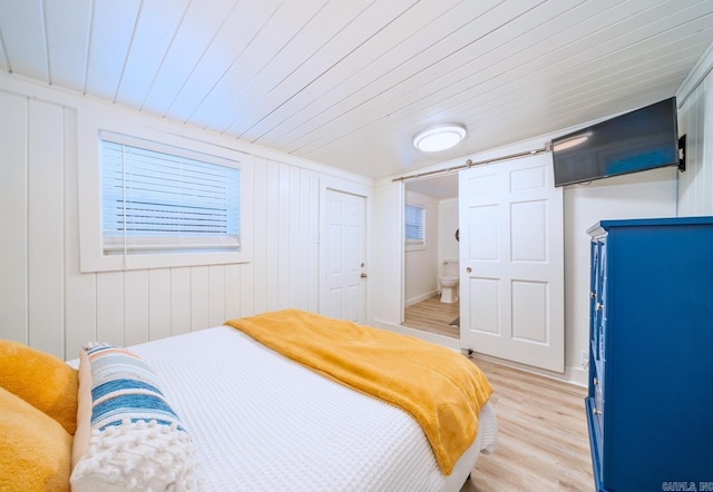 bedroom with light hardwood / wood-style floors, wooden ceiling, ensuite bath, and a barn door