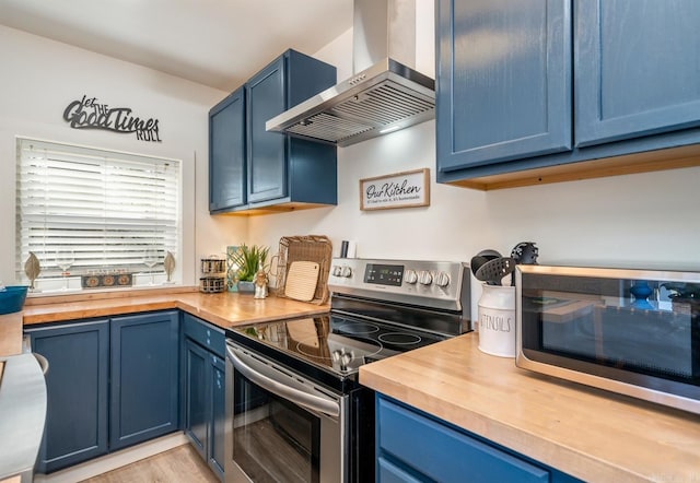 kitchen featuring stainless steel appliances, wall chimney exhaust hood, wooden counters, and blue cabinets