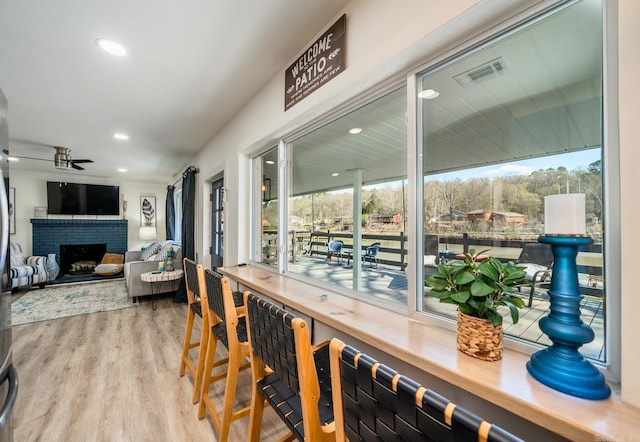 dining room with ceiling fan, a brick fireplace, wood finished floors, and a wealth of natural light